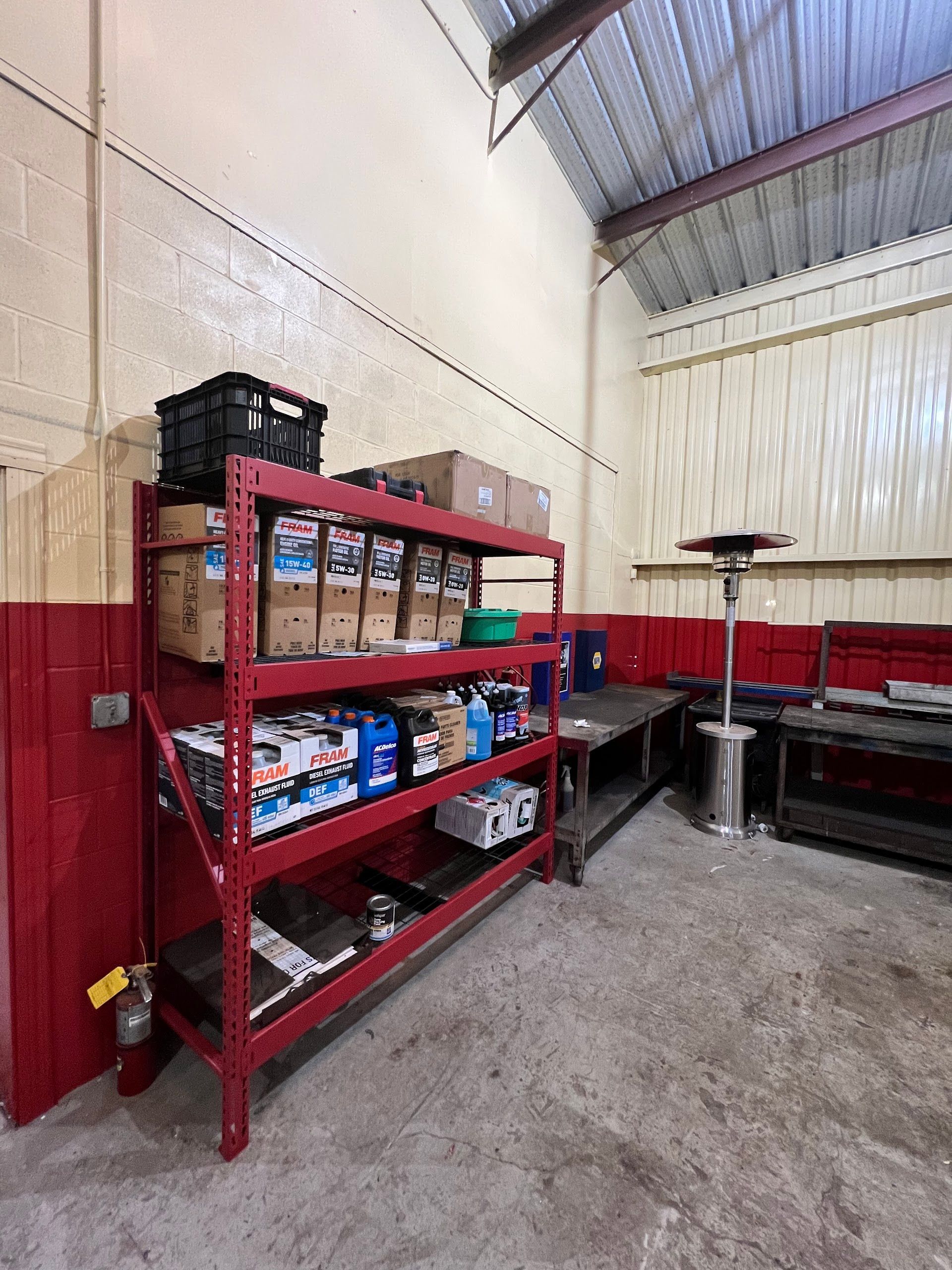 A red metal storage rack filled with boxes and supplies stands against a warehouse wall next to a tall patio heater. | Keep It Rollin’ Auto Repair LLC