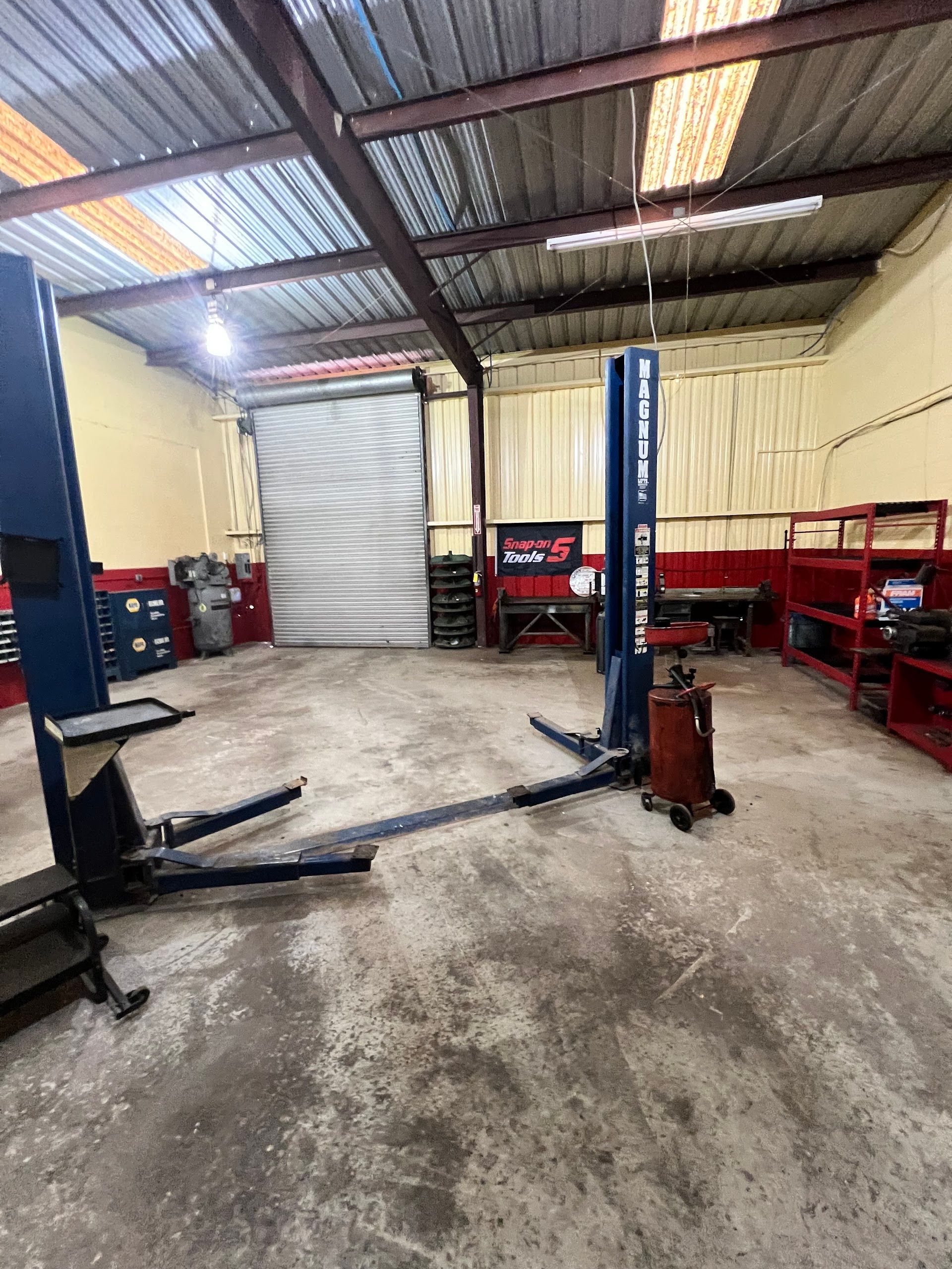 An empty auto repair workshop featuring a blue two-post vehicle lift in the center and red storage shelving on the right. | Keep It Rollin’ Auto Repair LLC