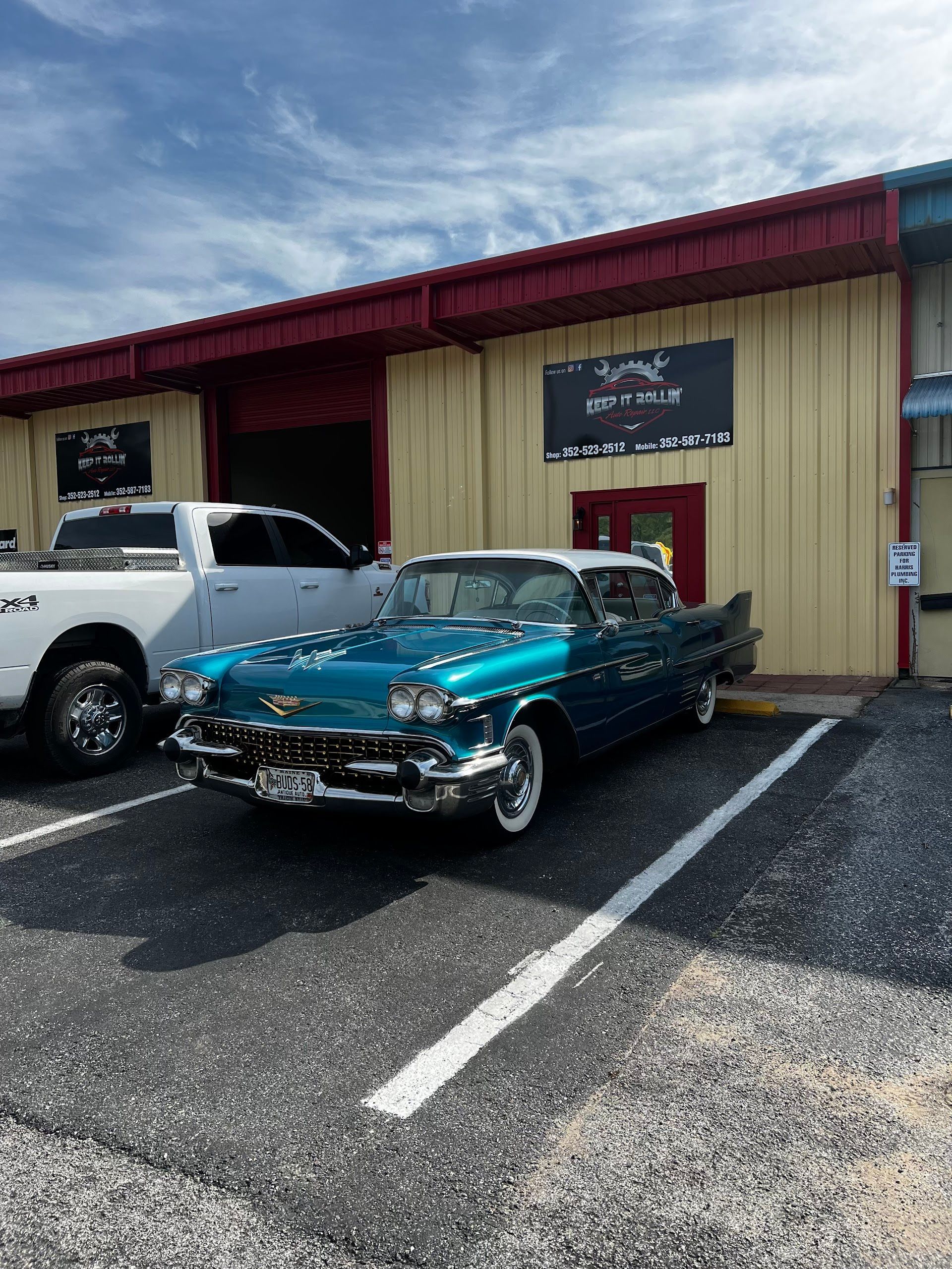 A teal vintage car parked in front of a metal warehouse building with a white pickup truck to its left. | Keep It Rollin’ Auto Repair LLC