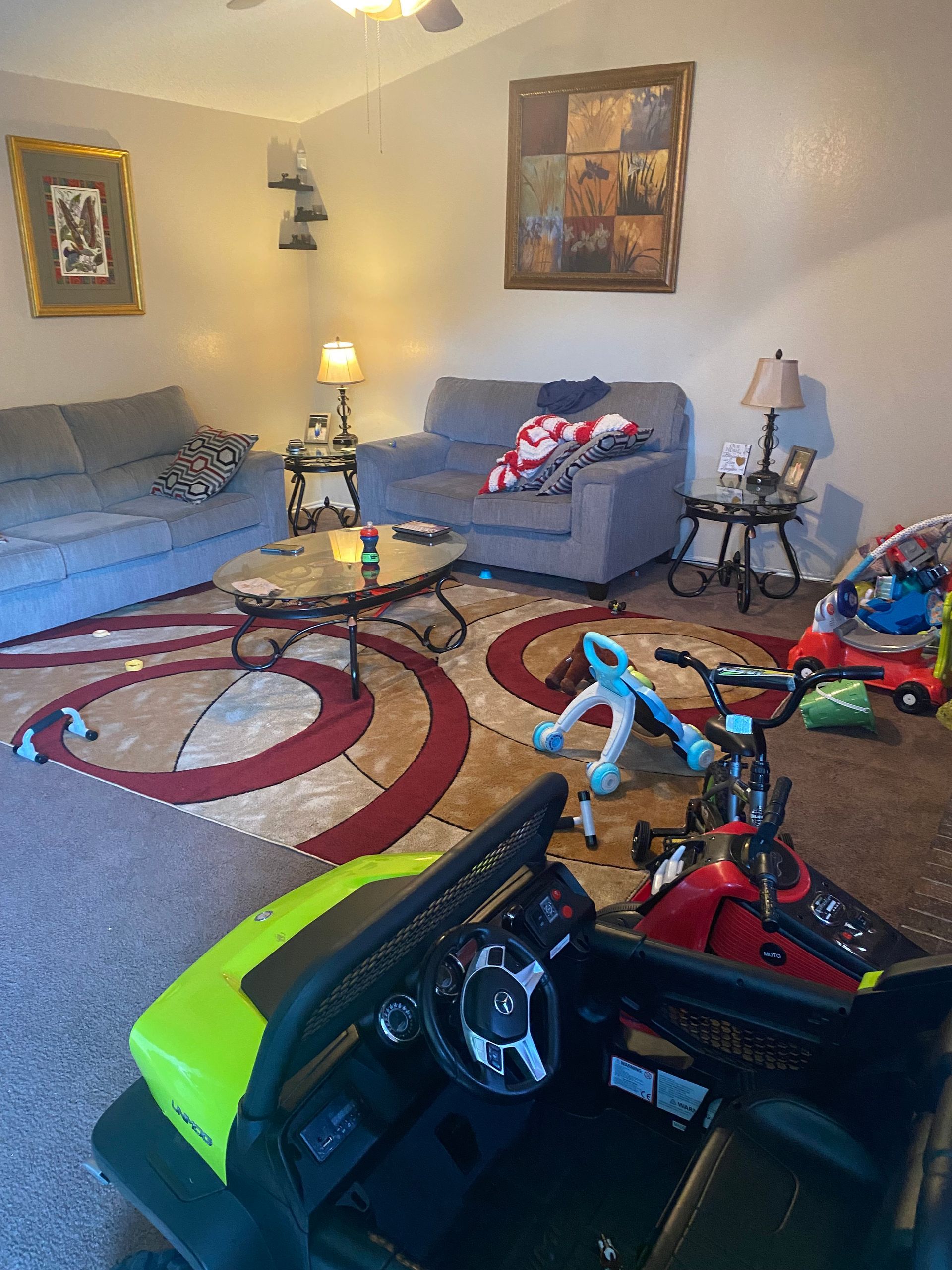 Living room with couches, rug, coffee table, lamps, and children's toys scattered on the floor.