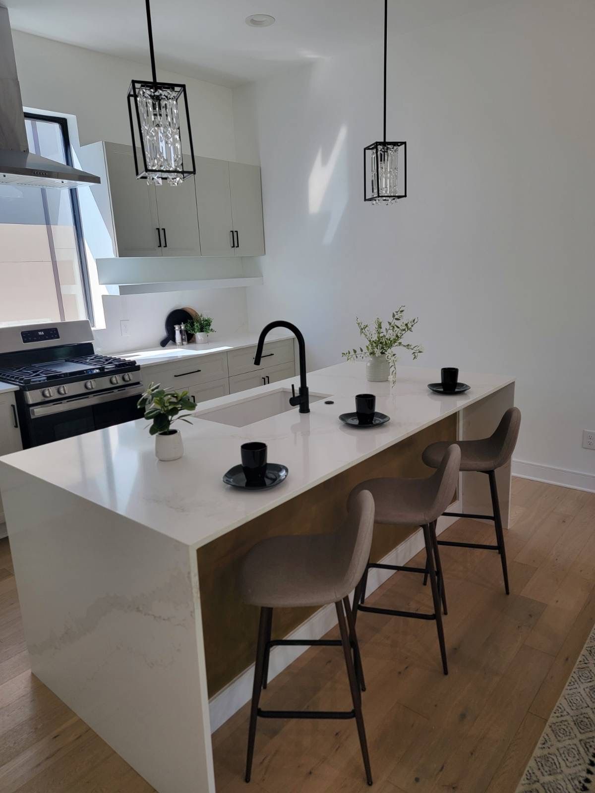Modern kitchen with island and three bar stools, featuring a sink, stovetop, and two pendant lights.