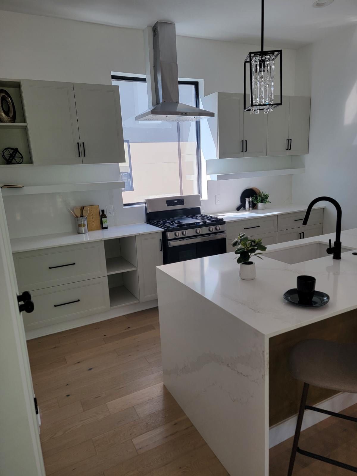Modern kitchen with light cabinets, stainless steel range hood, island, and wood floors.