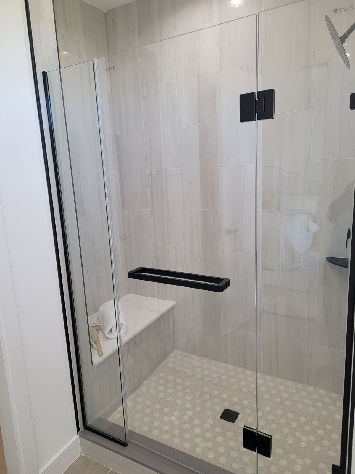 Glass shower stall with black hardware and white and gray tile.