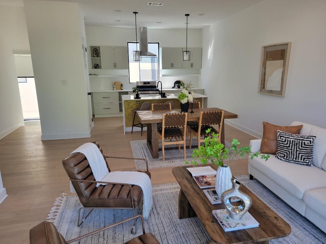 Bright, open-concept living space with dining area, kitchen, and seating area featuring neutral tones and wood accents.