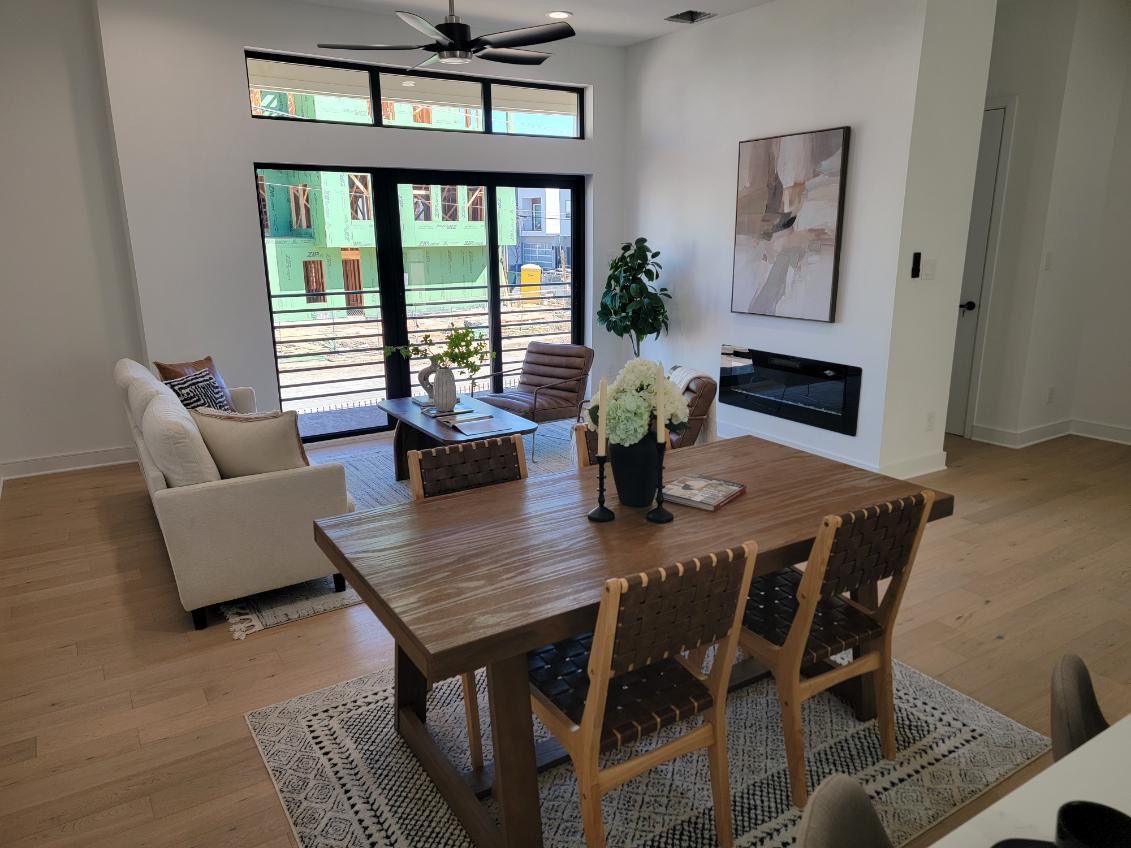Living room with a wooden dining table, sofa, fireplace, and large windows.