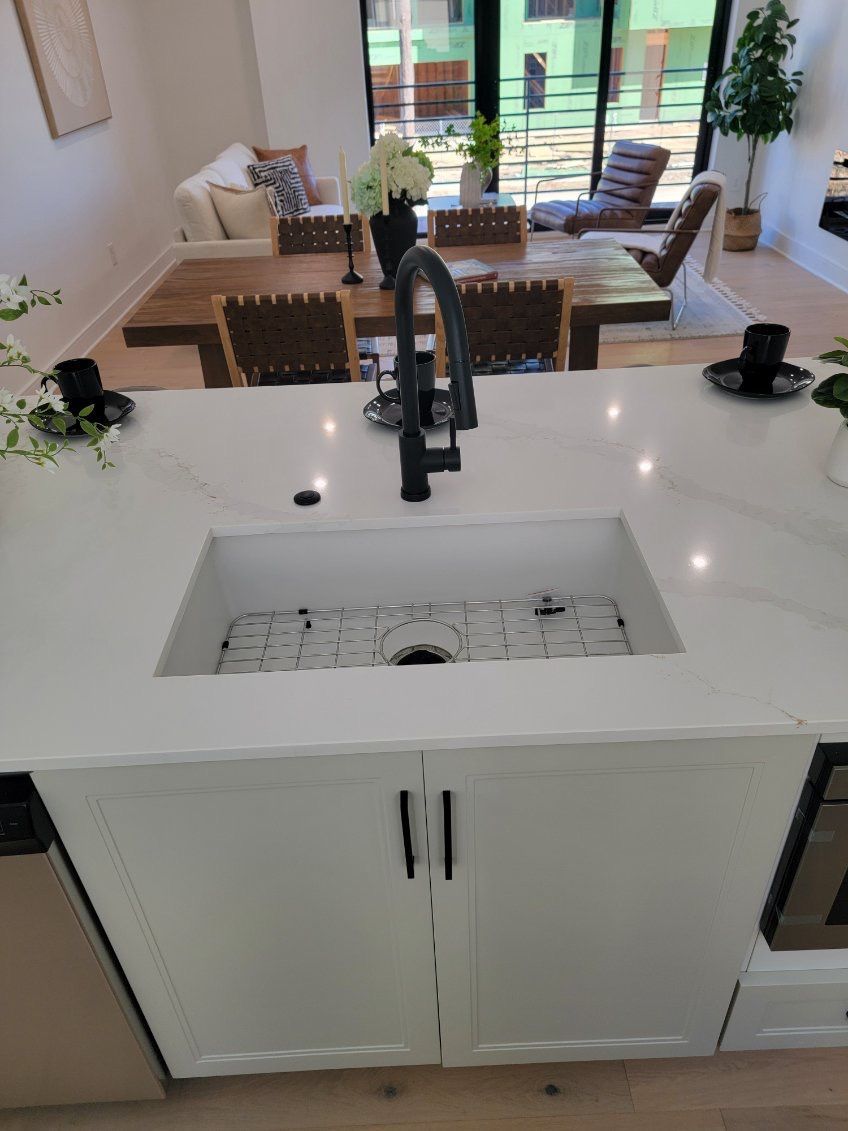 Kitchen island with white cabinets, marble countertop, black faucet, and sink. Dining room visible in background.