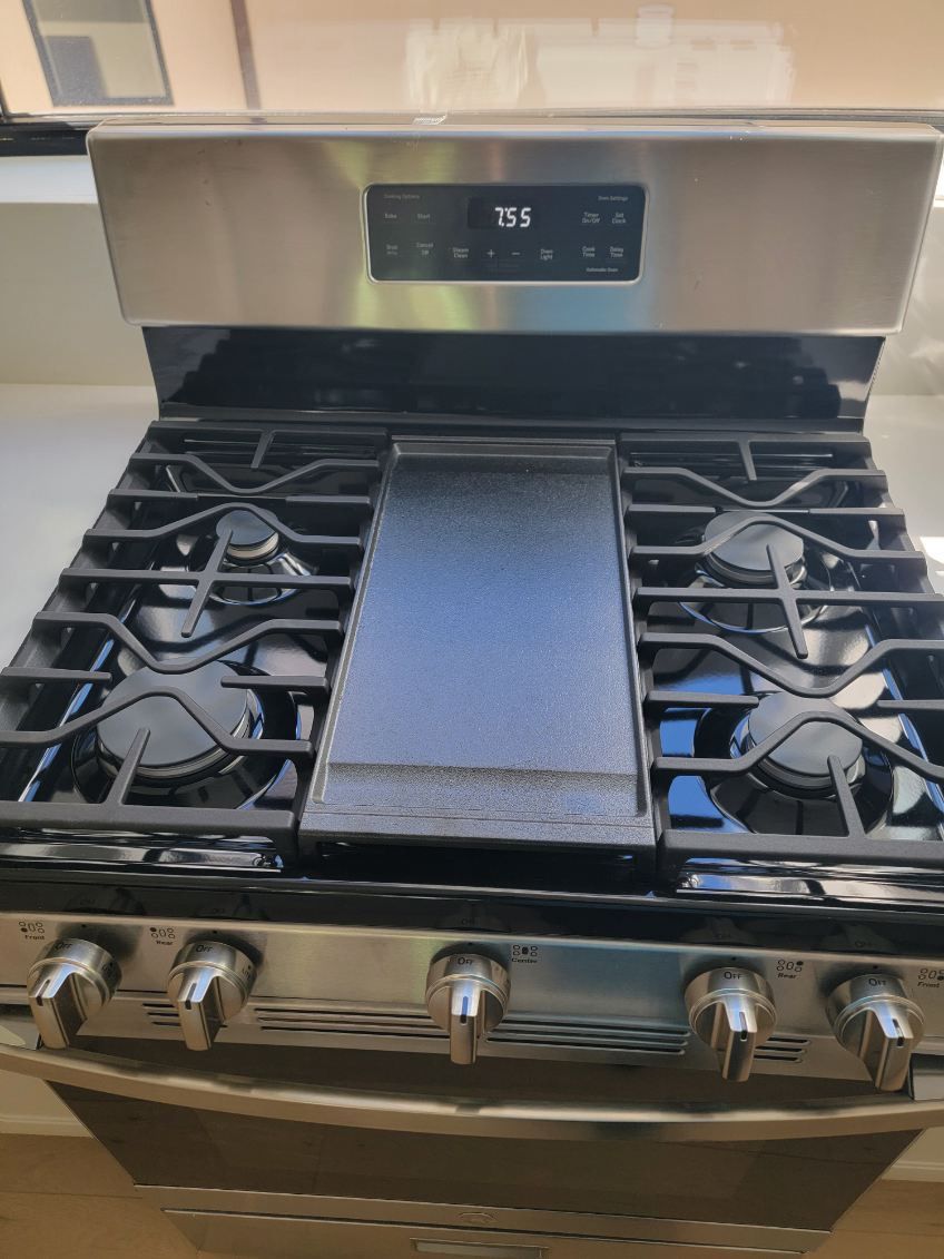 Stainless steel gas range with black grates, griddle, and control panel.