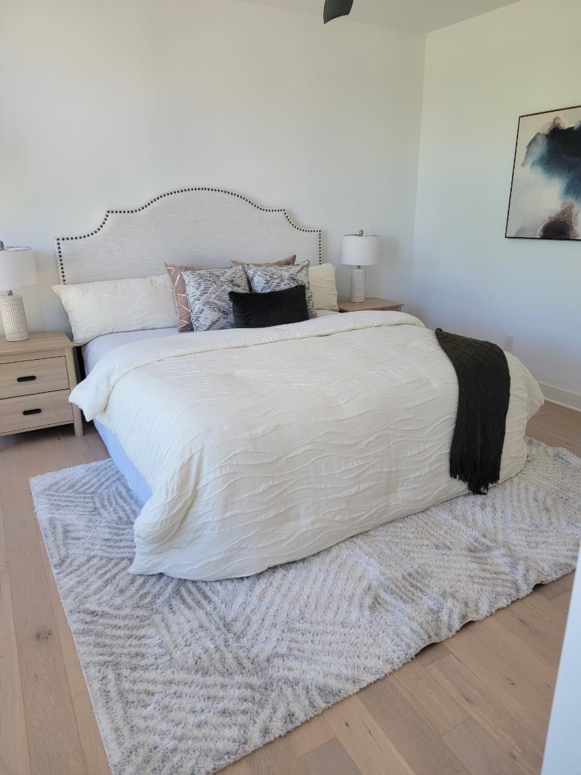 Bedroom with a white bed, patterned rug, and artwork on a white wall.