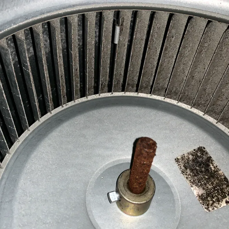 Dusty HVAC blower fan with gray blades and a rusty-looking center.
