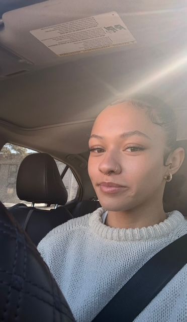 Person sitting in a car, wearing a gray sweater and seatbelt, with sunlight streaming in.