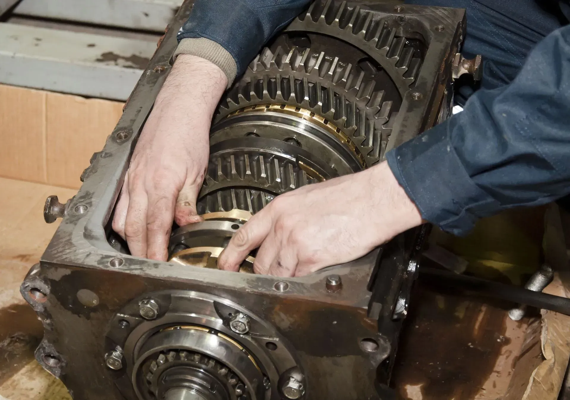 Hands inspecting the gears inside a large metal gearbox on a workbench