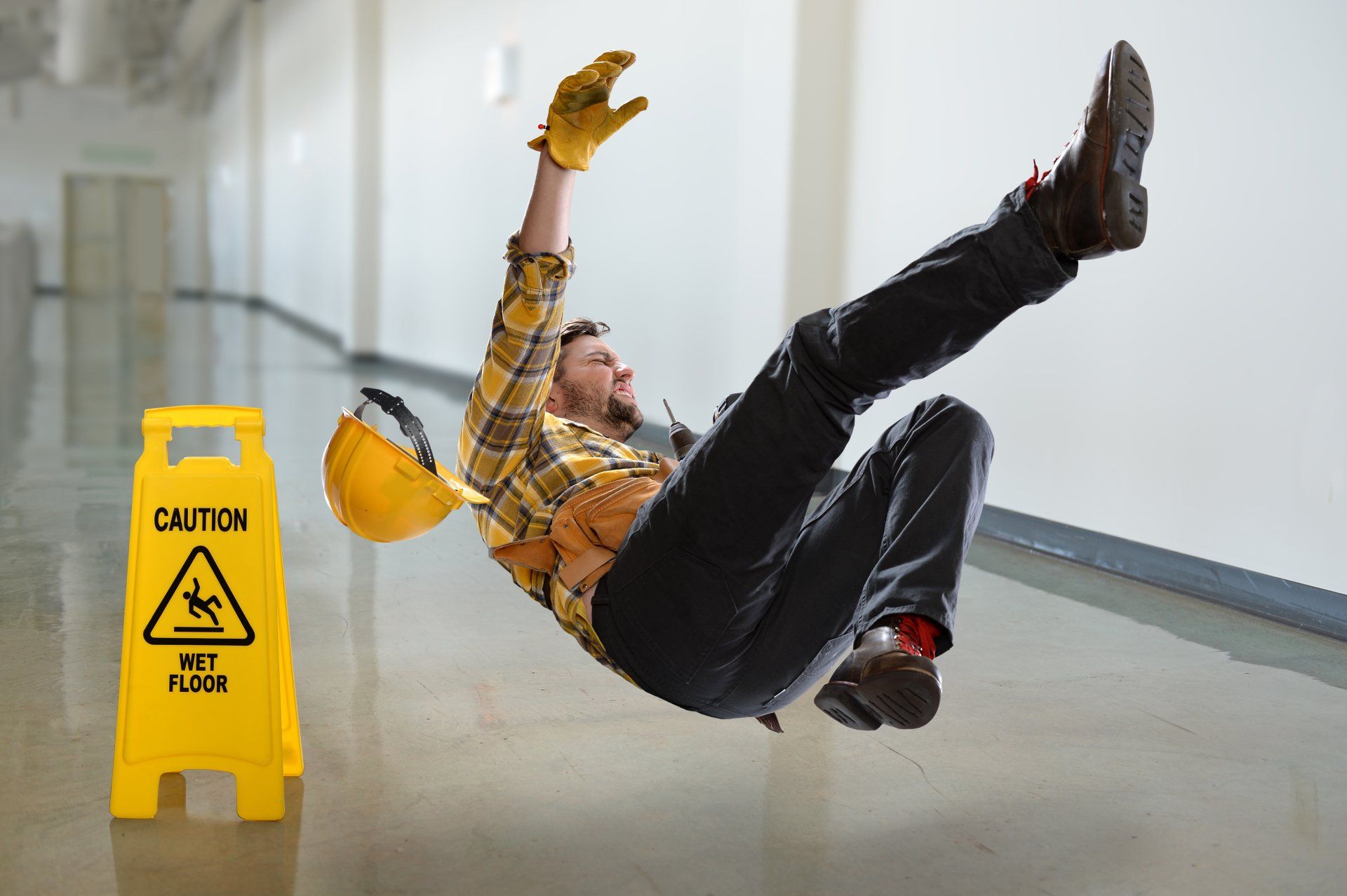 a man is falling on a wet floor next to a caution sign .