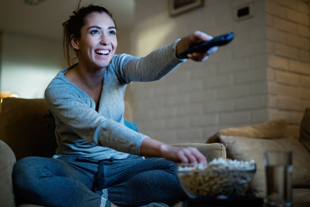 A Woman Is Sitting On A Couch Holding A Remote Control — Craig's TV/Antenna Services In Maryland, NSW