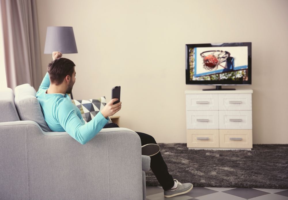 A Man Is Sitting On A Couch Watching A Basketball Game On A Television — Craig's TV/Antenna Services In Cameron Park, NSW