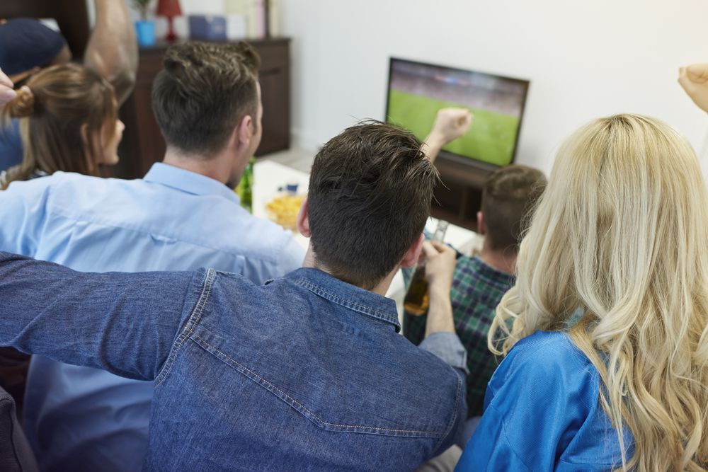 A Group Of People Are Sitting On A Couch Watching A Television — Craig's TV/Antenna Services In Cardiff, NSW