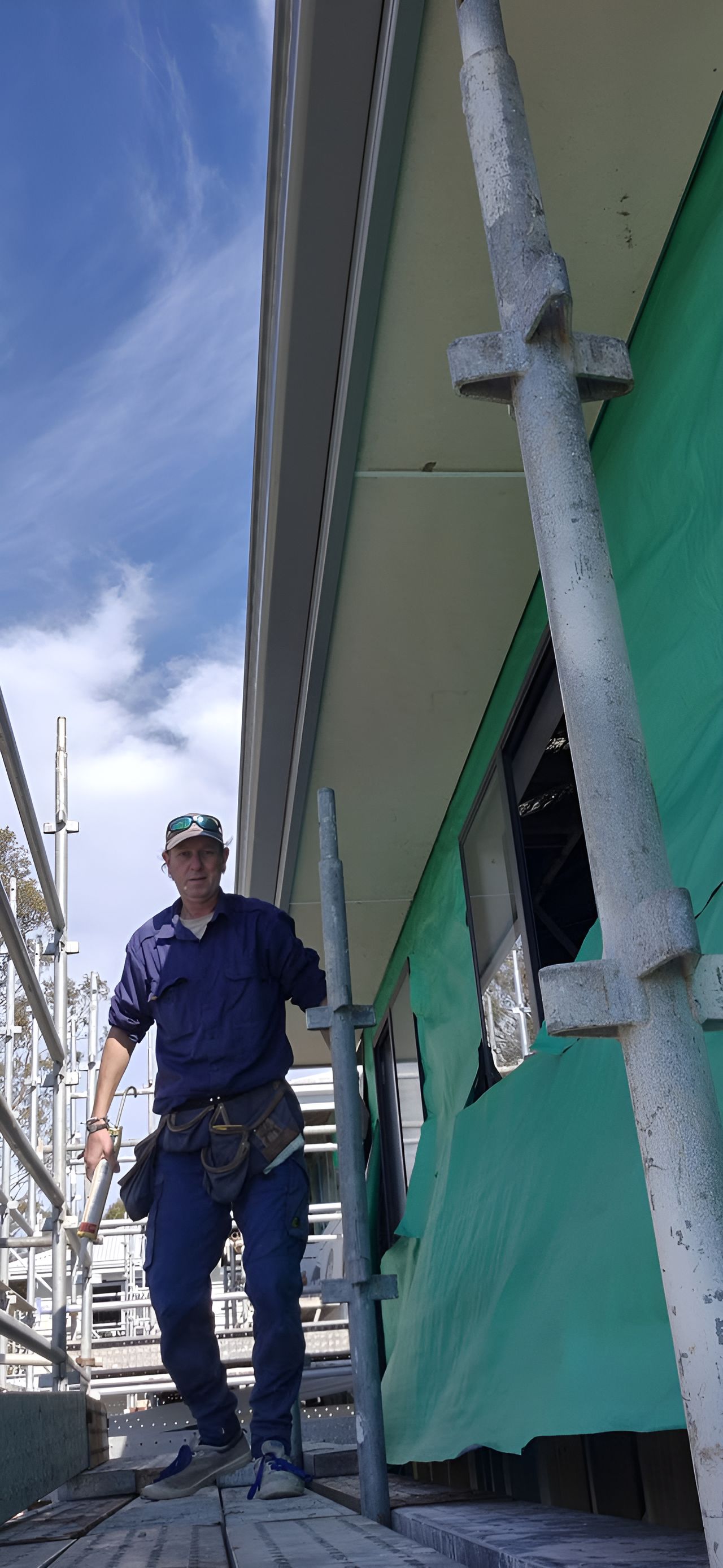 A Man Is Standing On A Scaffolding Next To A Building — Craig's TV/Antenna Services In Cardiff, NSW