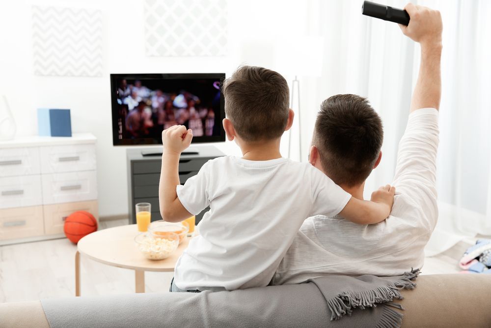 A Man And A Boy Are Sitting On A Couch Watching A Television — Craig's TV/Antenna Services In Newcastle, NSW