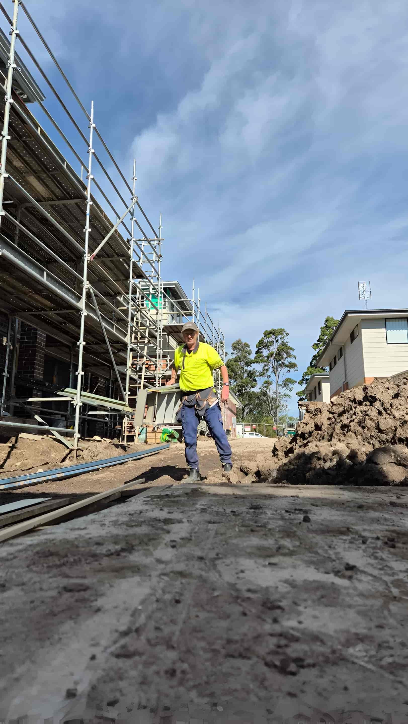 A Man Is Standing On A Dirt Road In Front Of A Building Under Construction — Craig's TV/Antenna Services In Maitland, NSW