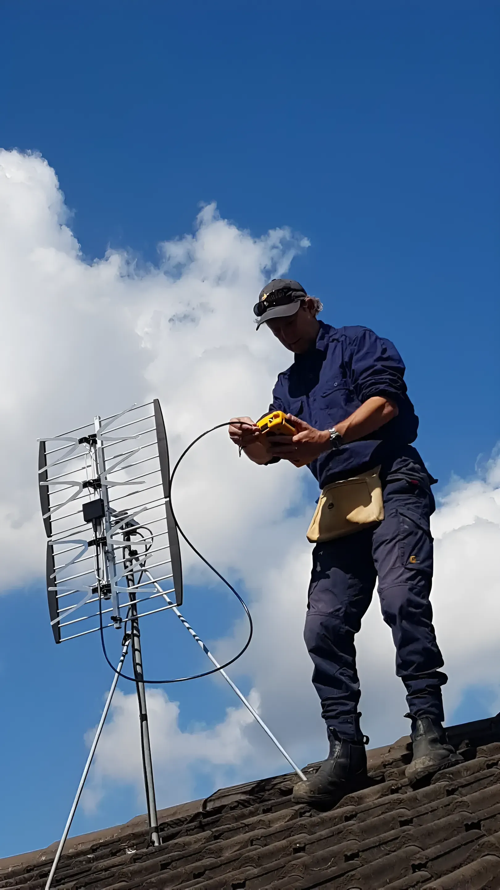 A Man Is Standing On Top Of A Roof Working On An Antenna — Craig's TV/Antenna Services In Merewether, NSW