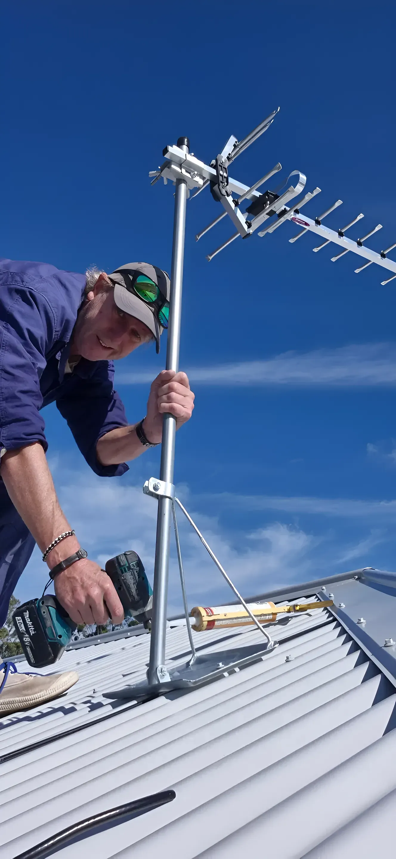 A Man Is Working On An Antenna On The Roof Of A Building — Craig's TV/Antenna Services In Cessnock, NSW