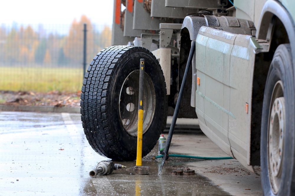 A Truck Tire Being Repaired with Tools on Wet Pavement — Aust. Advanced Trailer Sales & Service in Berrimah, NT