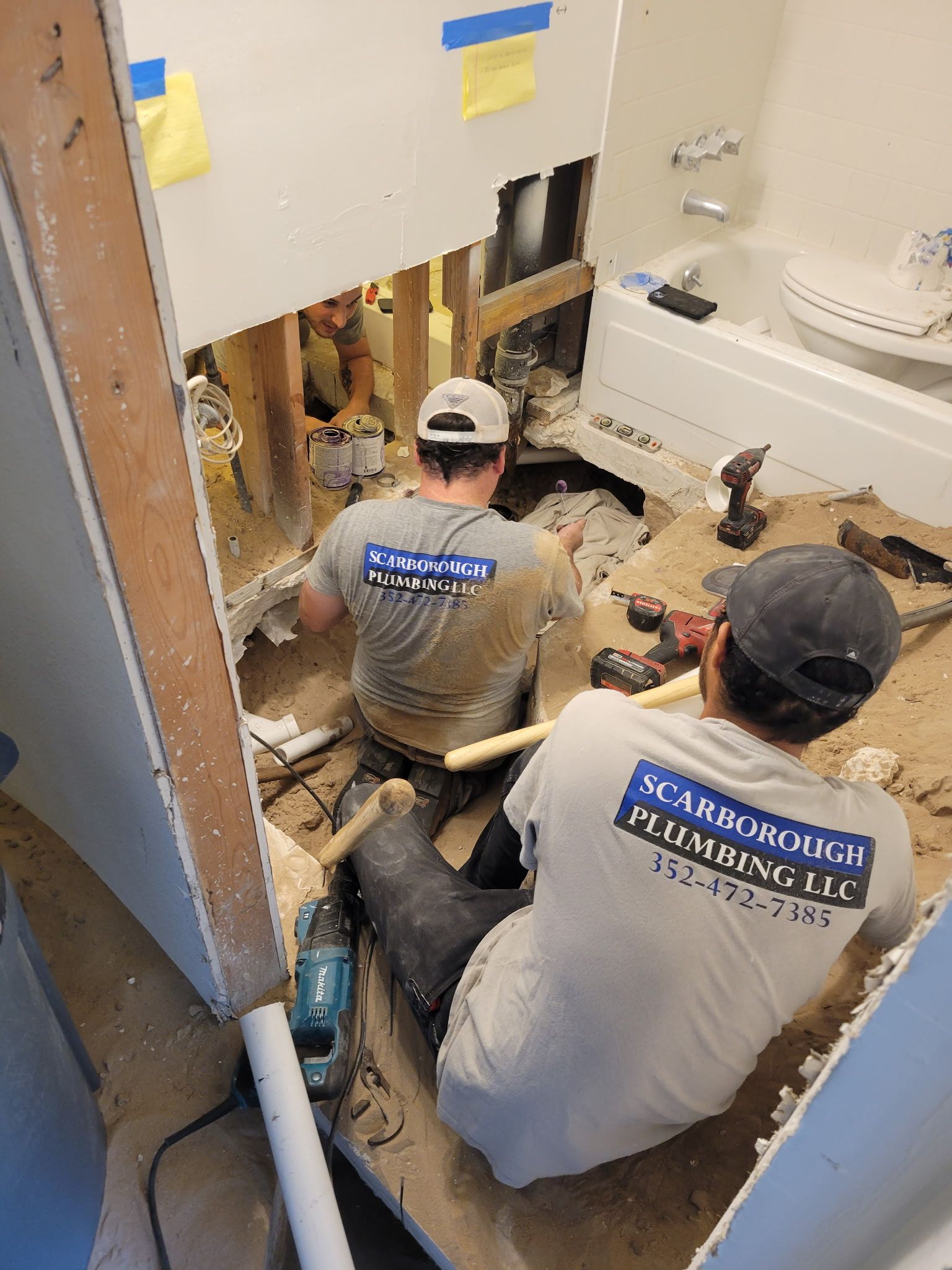 Two plumbers working on bathroom renovation, tearing up walls and floor.