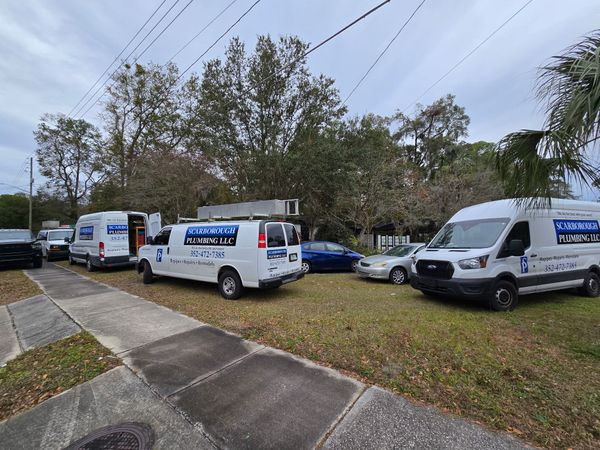 Several white work vans with logos parked on a grassy area along a residential street.