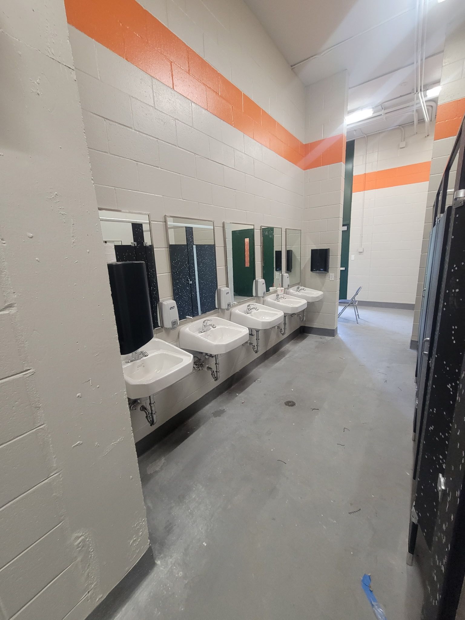 Public restroom with several sinks and mirrors. Orange stripe on top of a gray wall.