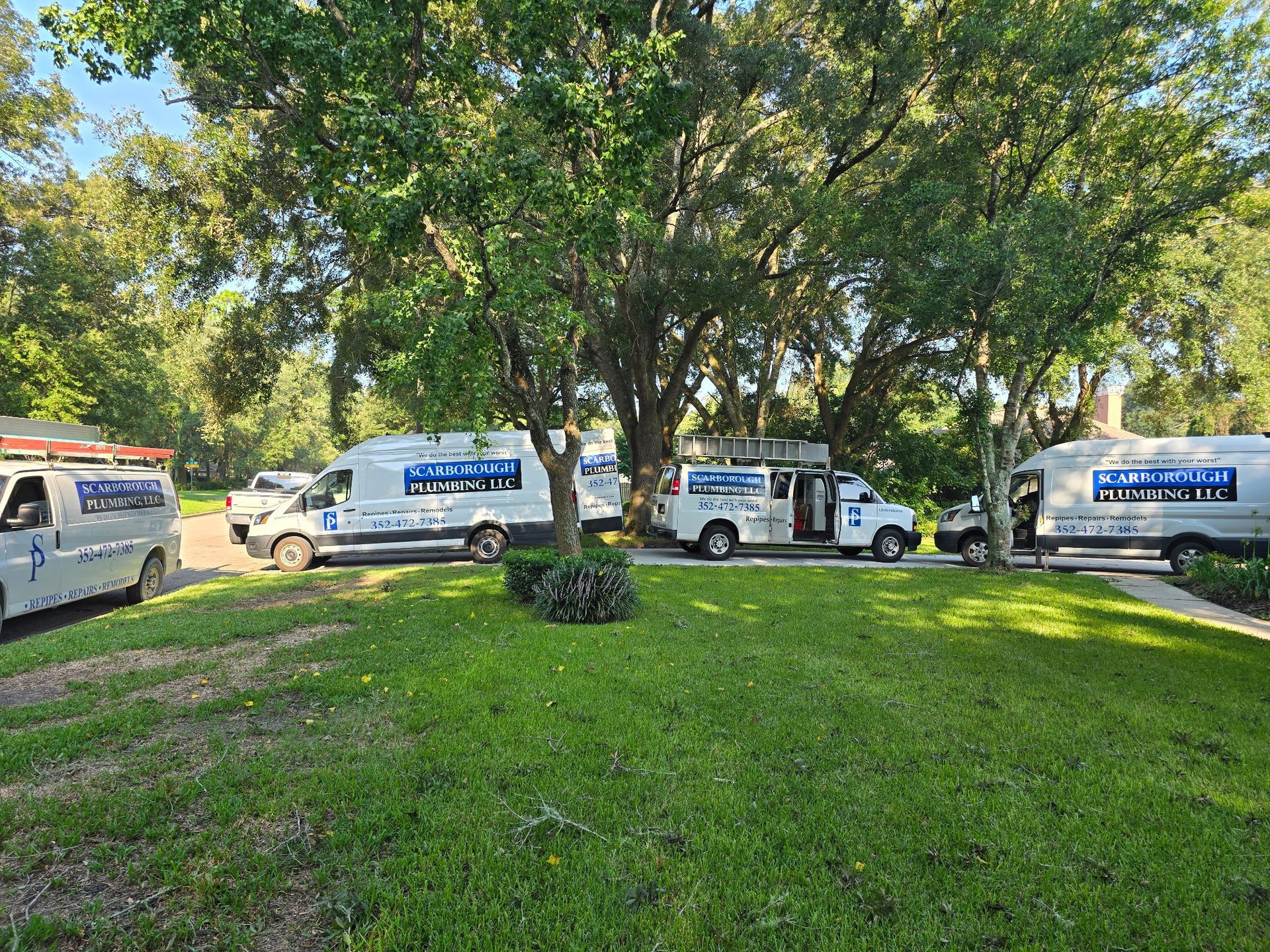 Several white service vans parked on grass under trees. Blue logo, open doors.