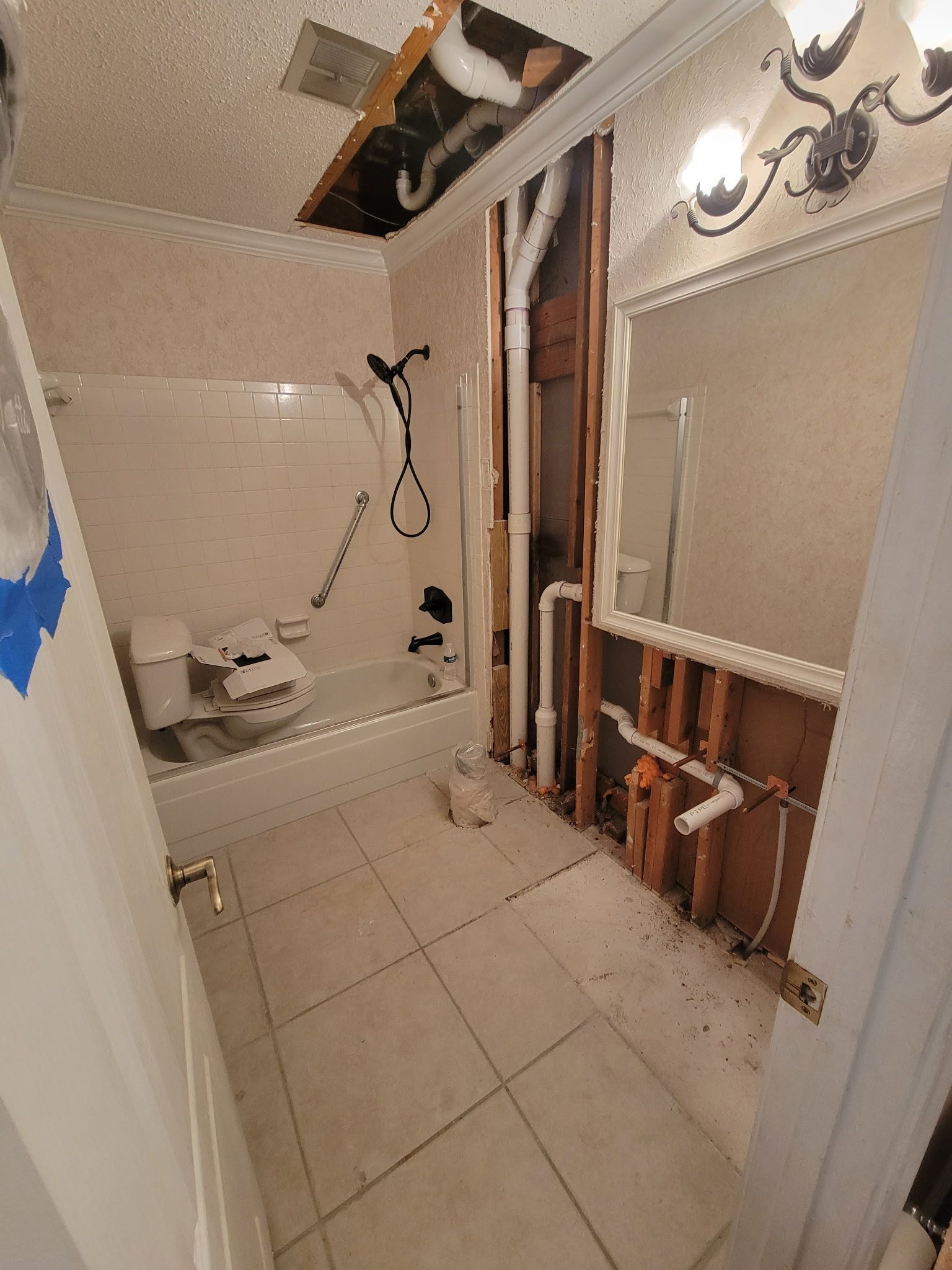 Partially gutted bathroom with exposed plumbing, broken wall panels, and tiled floor under renovation