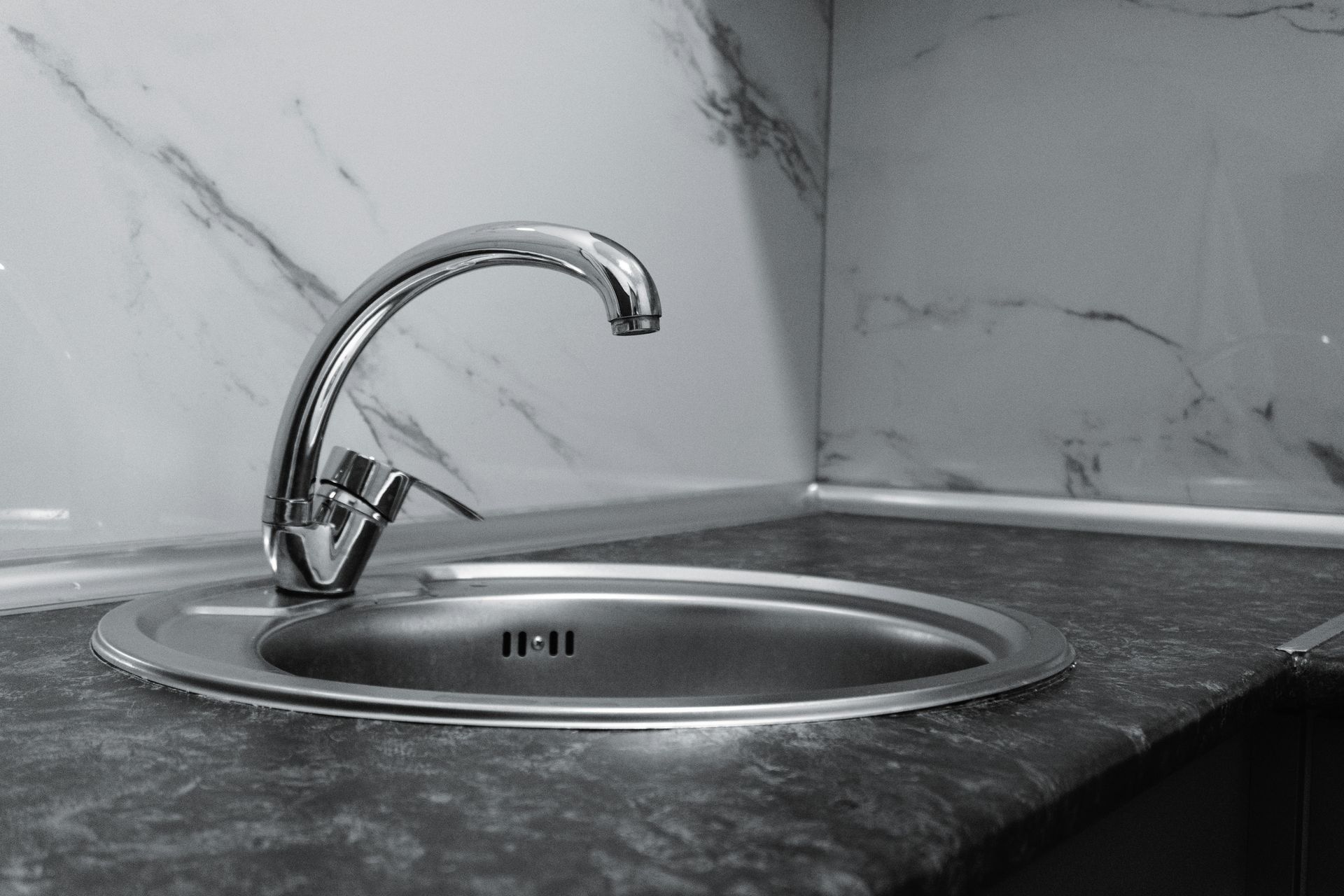 Stainless steel sink with chrome faucet against a marble-patterned backsplash and countertop.