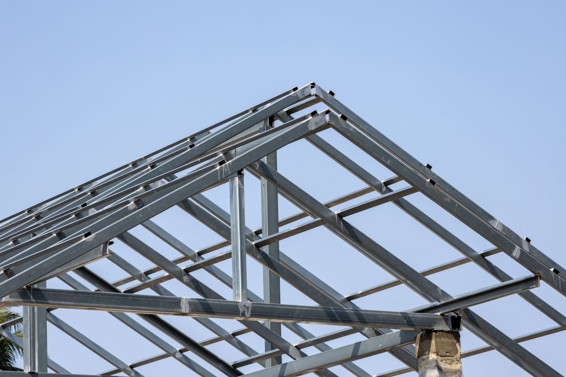 Steel roof frame under construction beneath clear blue sky.