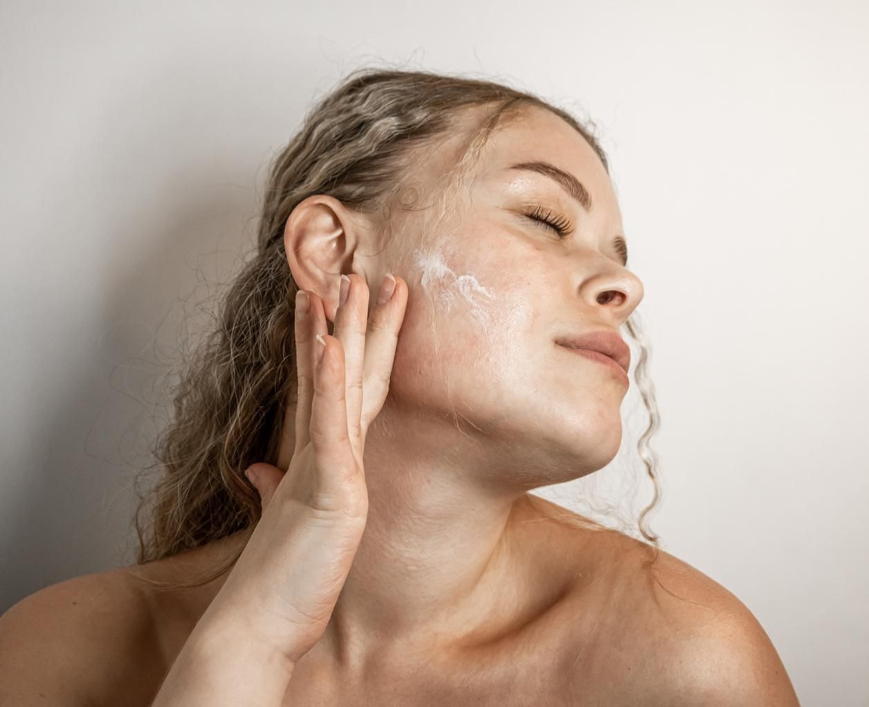 Woman applying moisturizer on her skin  contemplating her skin care products and facial treatments.