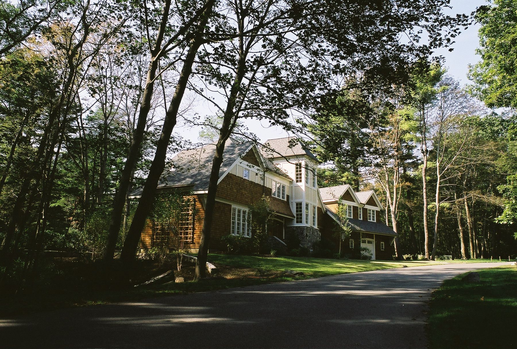 Large house nestled in a grove of trees, seen from a paved driveway.
