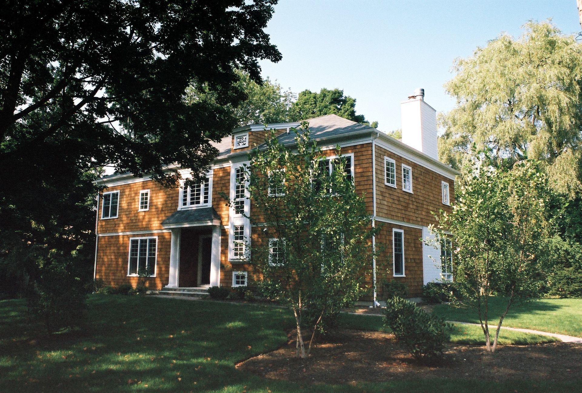 Two-story brick house with a white trim and chimney, set on a grassy lawn with trees.