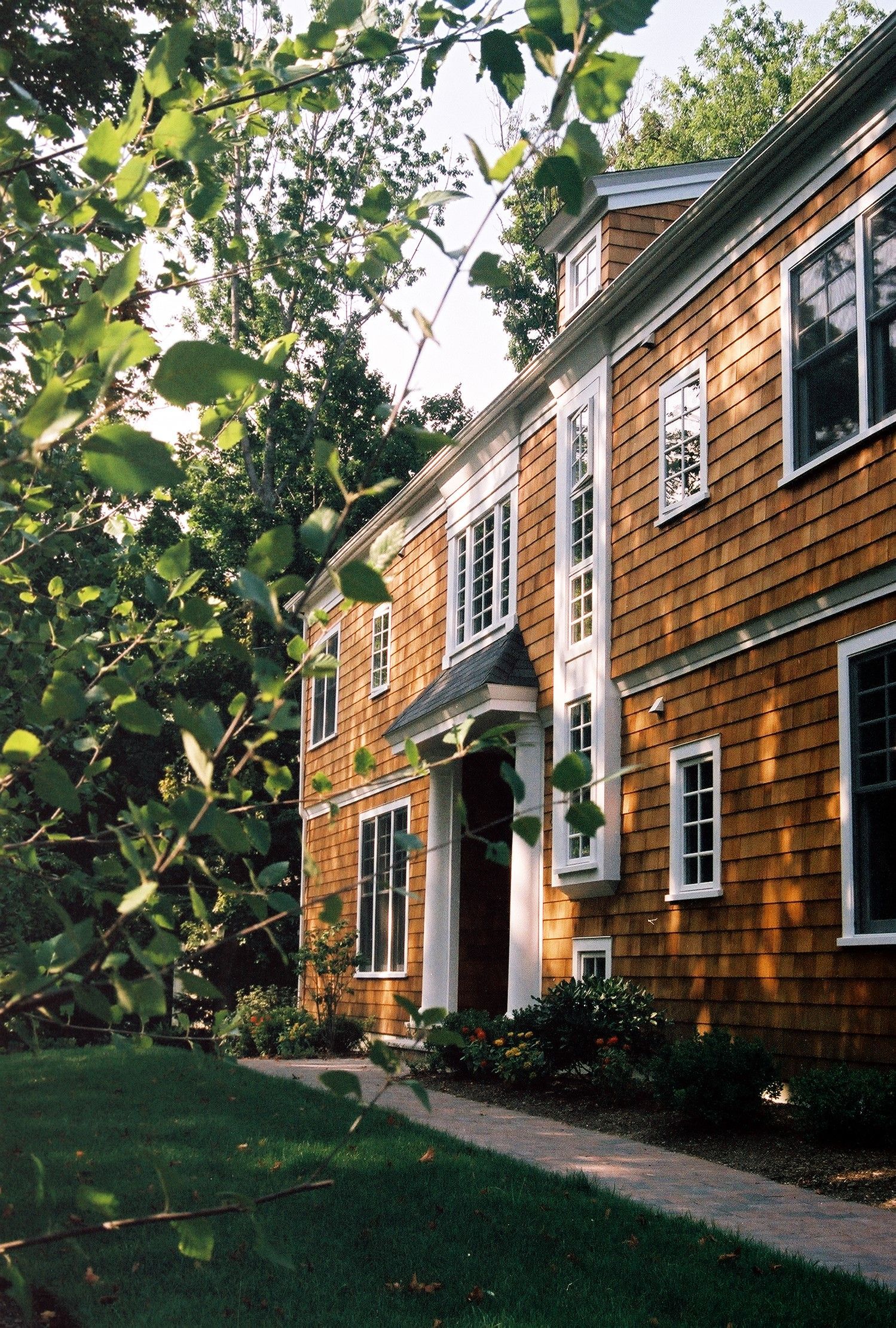 Two-story, cedar-shingled building with white trim, a walkway, and surrounding greenery.
