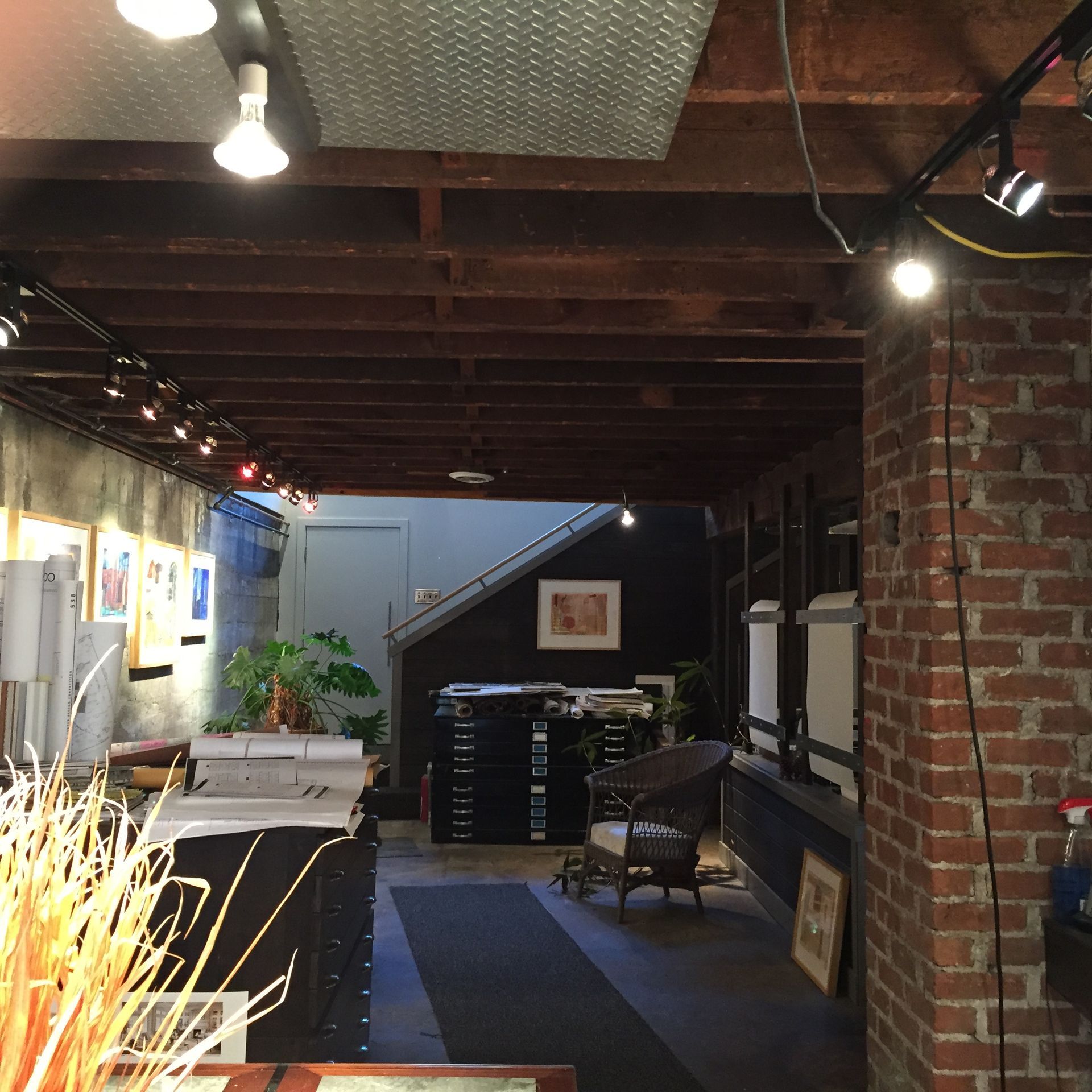 An art gallery interior with exposed brick and wood, artwork on display, and various equipment.