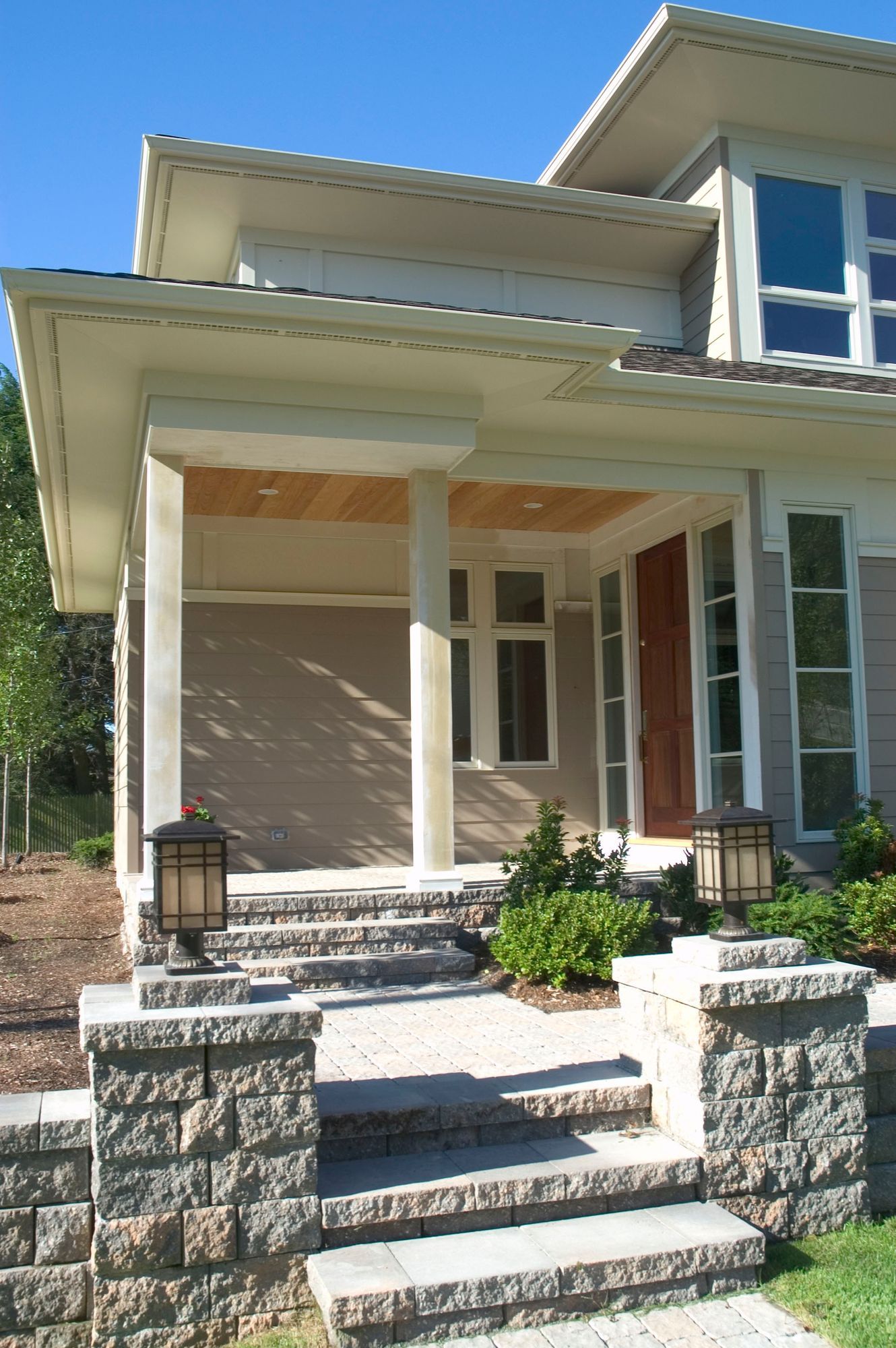 Stone steps lead up to a modern home's covered porch, with pillars and lanterns.