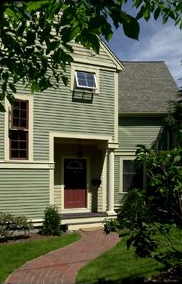 Two-story green house with a red door, windows open, and a brick walkway leading to the entrance.
