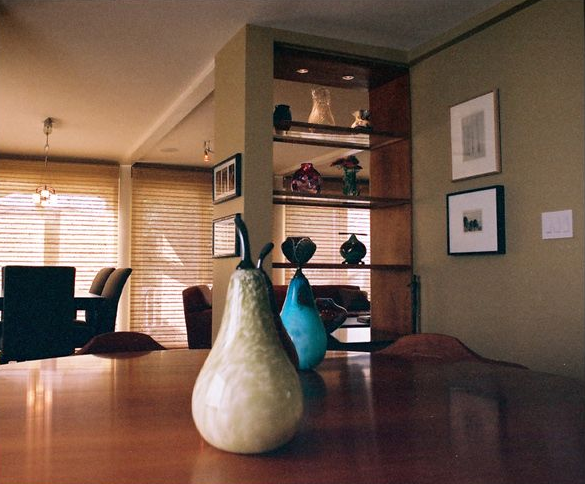 Wooden dining table with pear-shaped figurines; open shelving unit with art; framed pictures on wall.