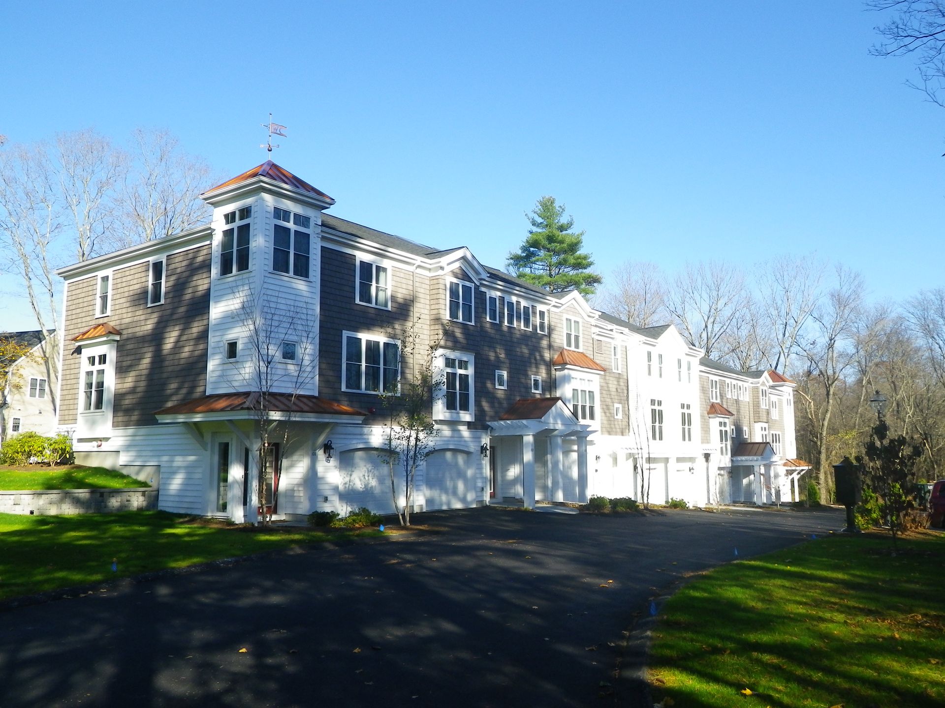 Row of multi-story townhouses with weathered gray siding, white trim, and attached garages on a sunny day.