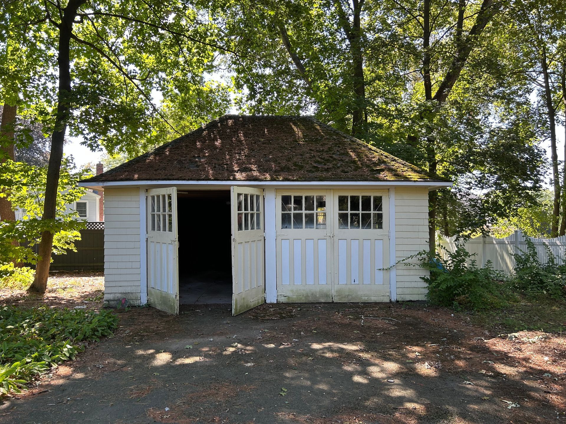 White wooden garage with open doors, surrounded by trees.