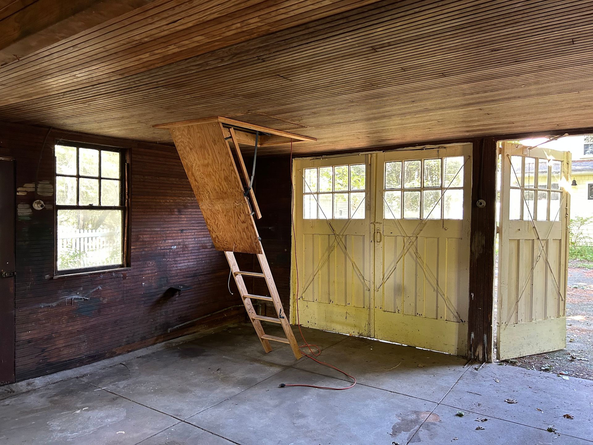 Garage interior with pull-down ladder to attic, two yellow garage doors open, and a window on the left.