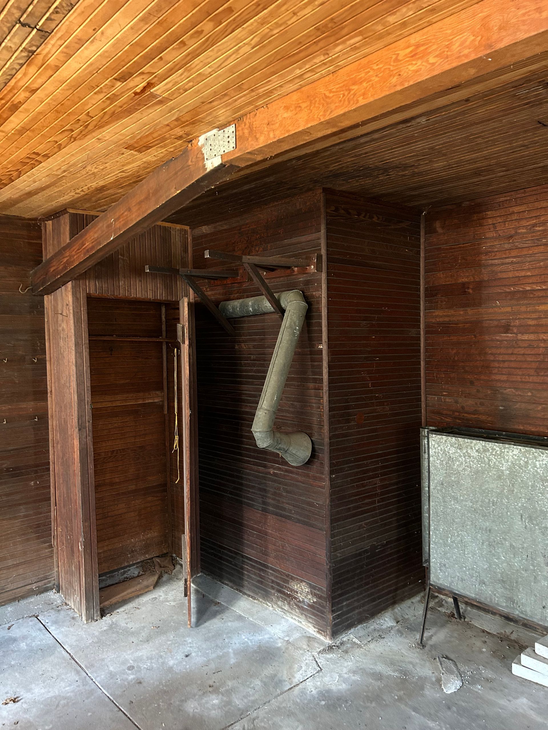 Interior of a wooden structure, possibly a shed, with a vent pipe and doorway visible.