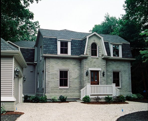 Gray stone house with dark gray roof, white trim, and a gravel driveway.