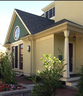 Yellow house with a green gable and a round window. A porch has white columns.