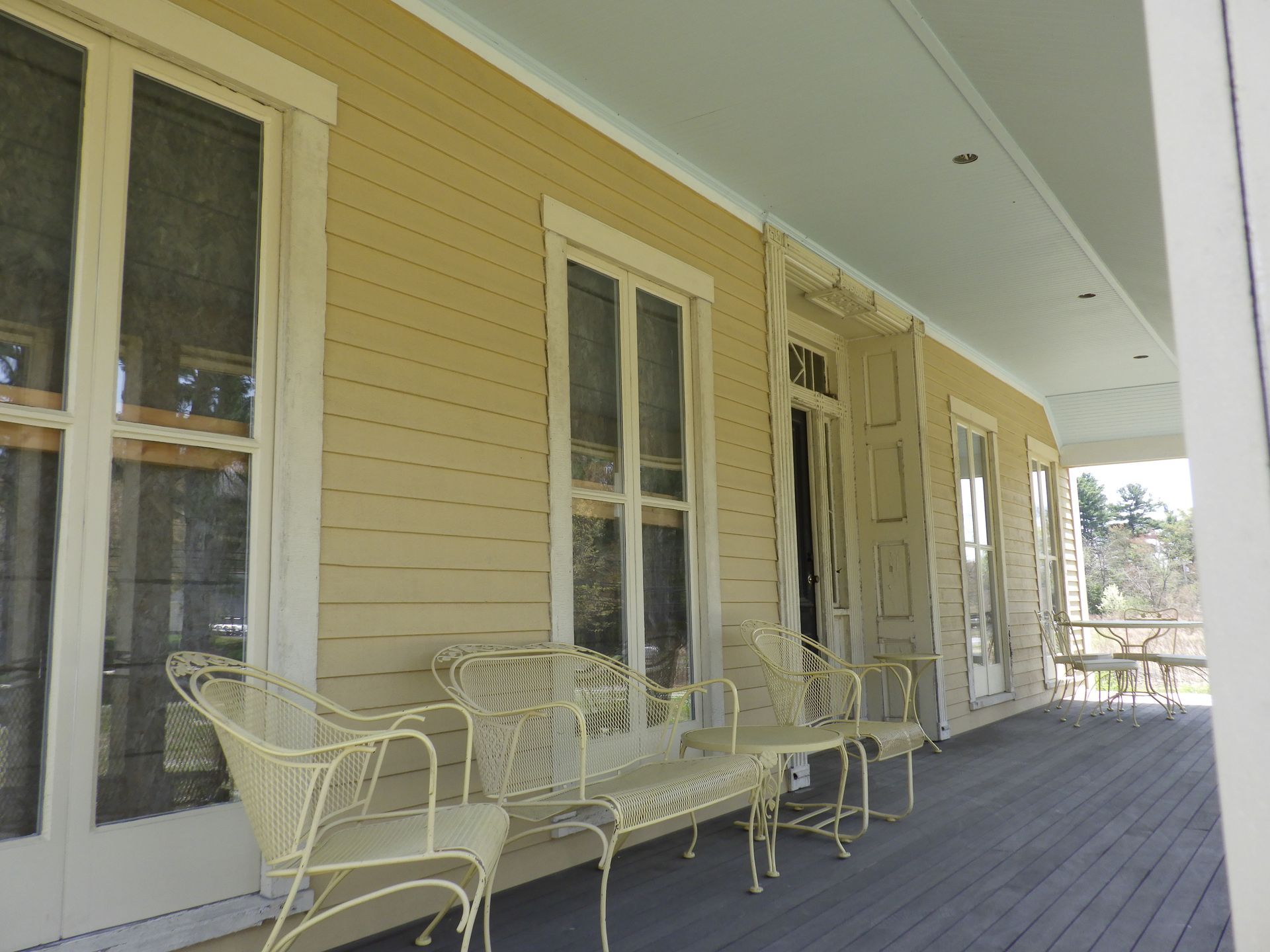 Covered porch with yellow siding and white trim.  Wicker furniture sits on the porch.