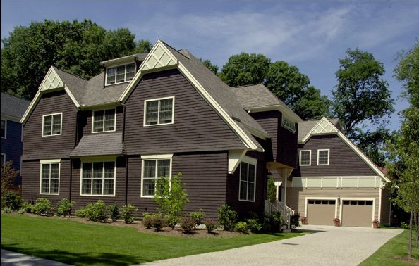 Brown two-story house with a garage, green lawn, and blue sky.