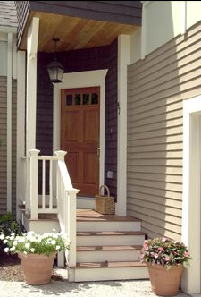 Front door entrance with steps, flower pots, and wooden door under a covered porch.