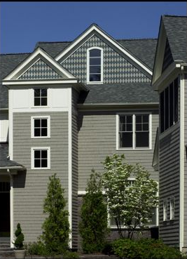 Gray house with multiple windows and a patterned gable, trees in front.